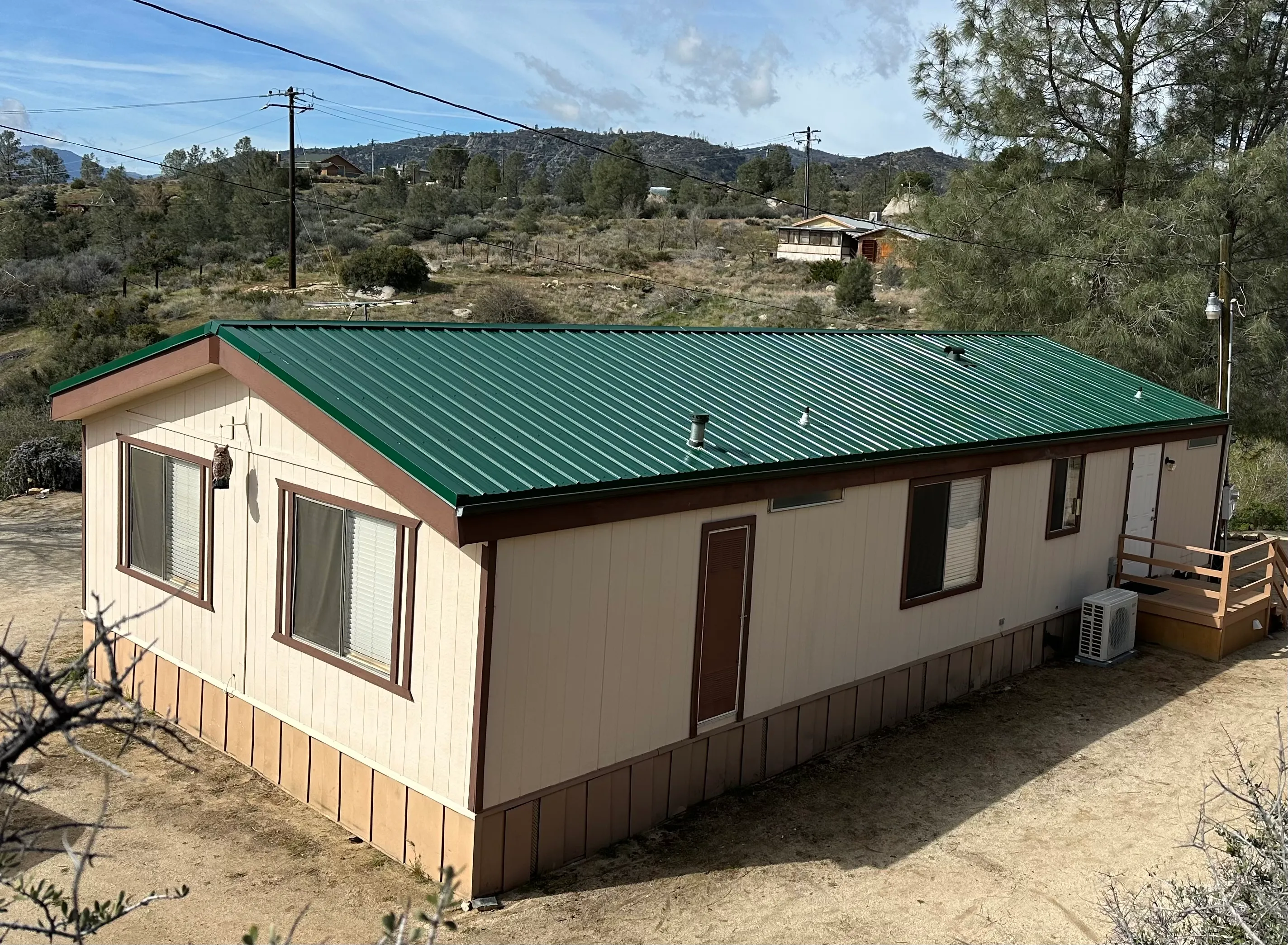 New green standing seam metal roof installed on a manufactured home in a rural foothill setting
